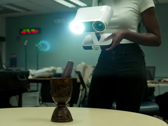 a person holding a lidar scanner with a camera lens and light scanning an mortar and pestle sitting on a table