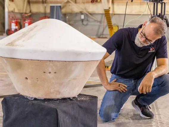A man crouches next to a replica of the flying saucer-like sample capsule.
