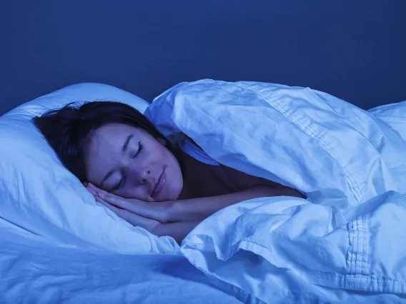 a person sleeping in a bed with white sheets under a soft blue light