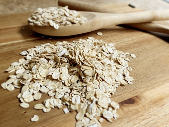A wooden spoon rests on a wooden table next to a pile of uncooked oats.