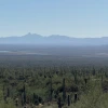 a midday, sunny view of a desert landscape with saguaros and distant ponds and a mountain ridgeline in the background 